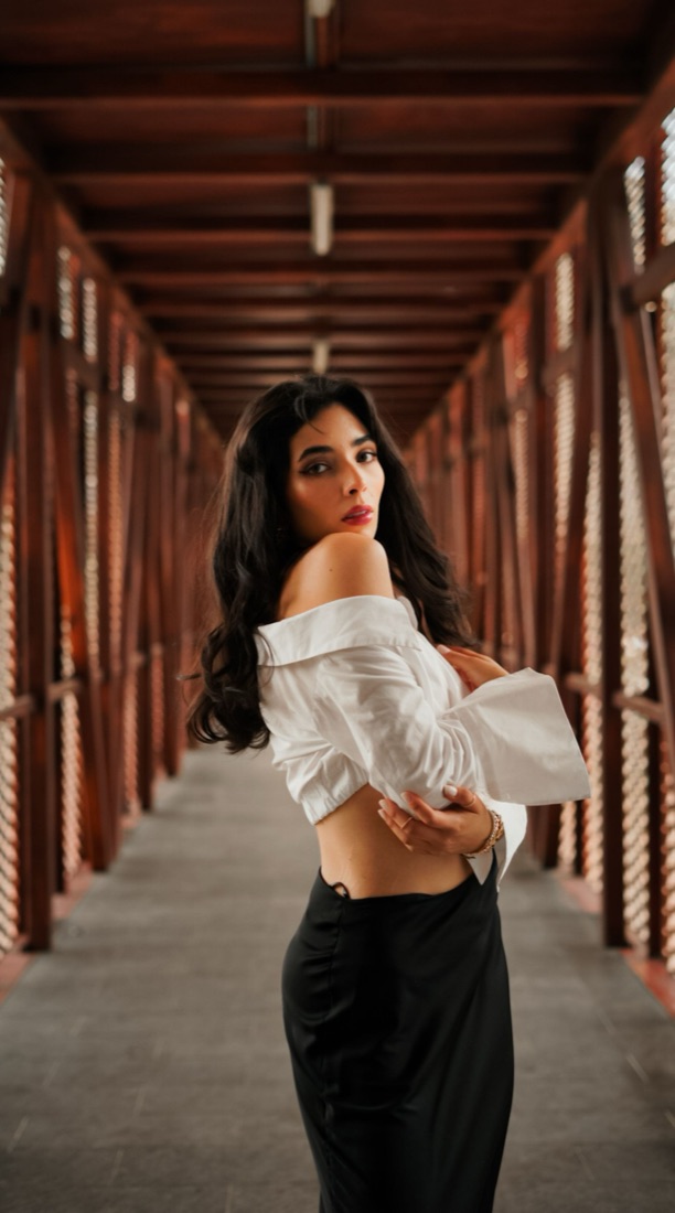 A woman in a white off-shoulder shirt looks back over her shoulder on a red metal footbridge.